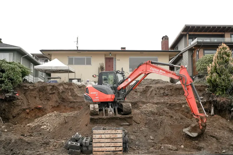 Red mini-excavator digging along the foundation wall of a house