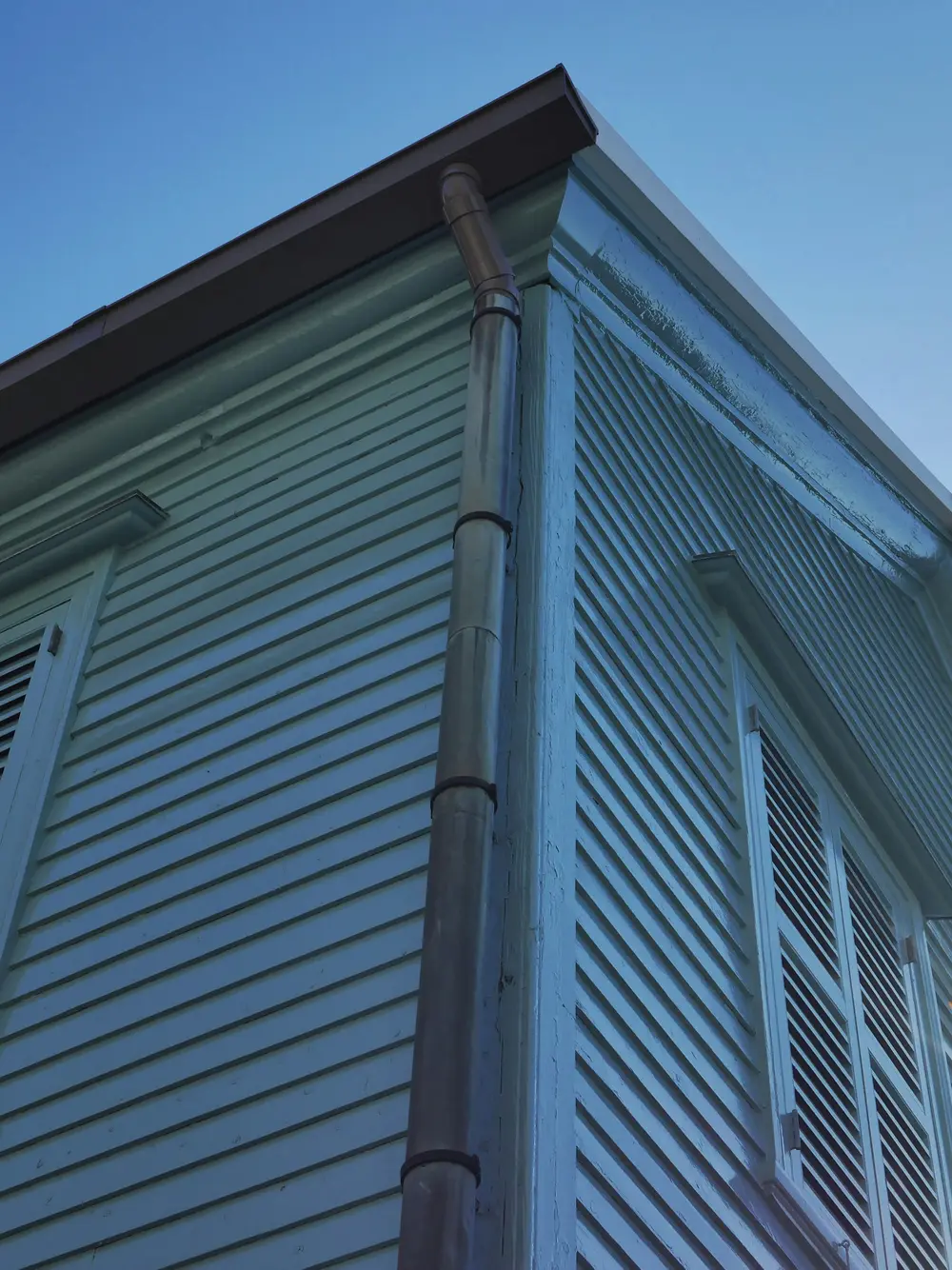 Downspout running down the corner of a house with grey siding