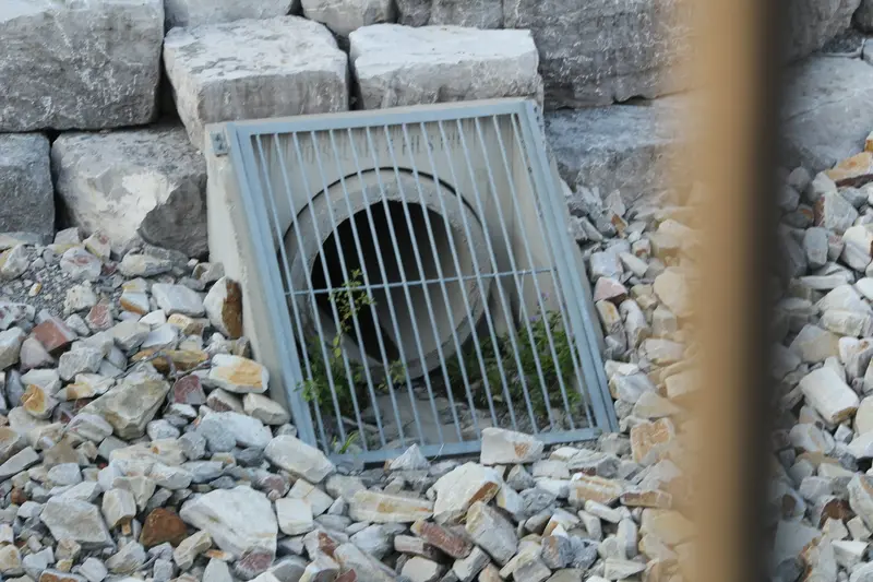 Drain outlet with a metal grate set in river stone where a discharge line reaches daylight