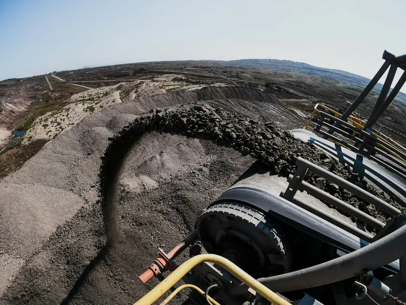 Excavator bucket dumping a load of dark soil during an excavation