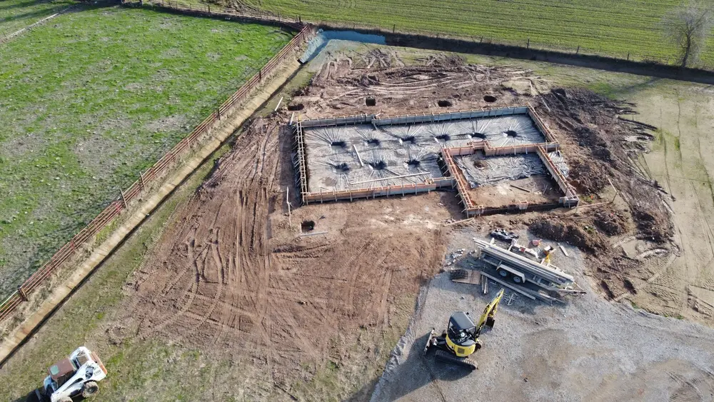 Aerial view of a house foundation excavation in an open field with an excavator on site
