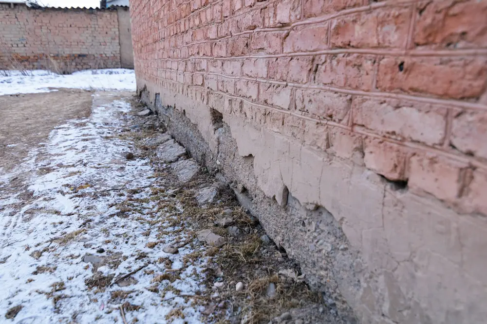 Base of a brick foundation wall at ground level with snow and ice against it