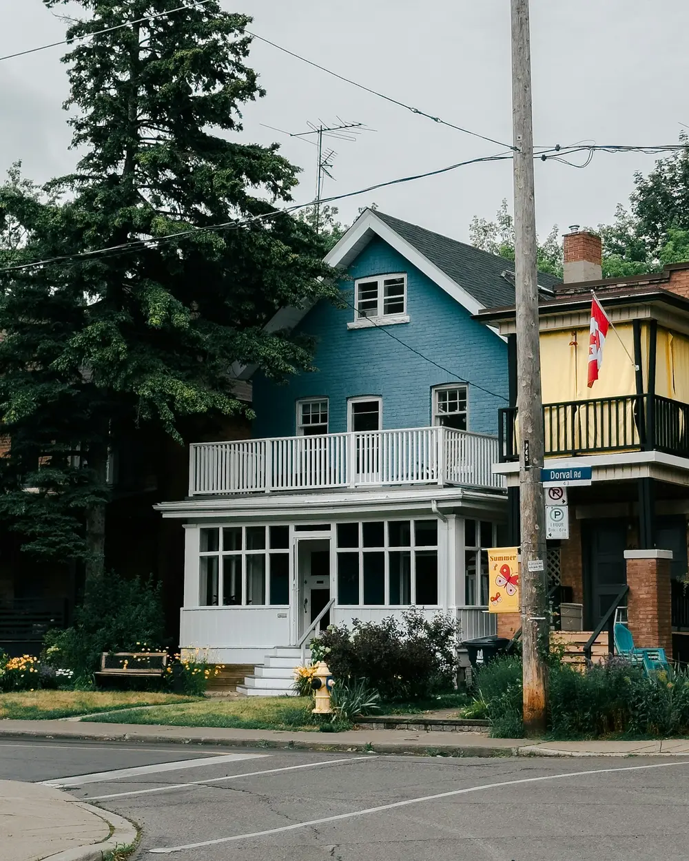 Blue two-storey house with a Canadian flag on a tree-lined residential street