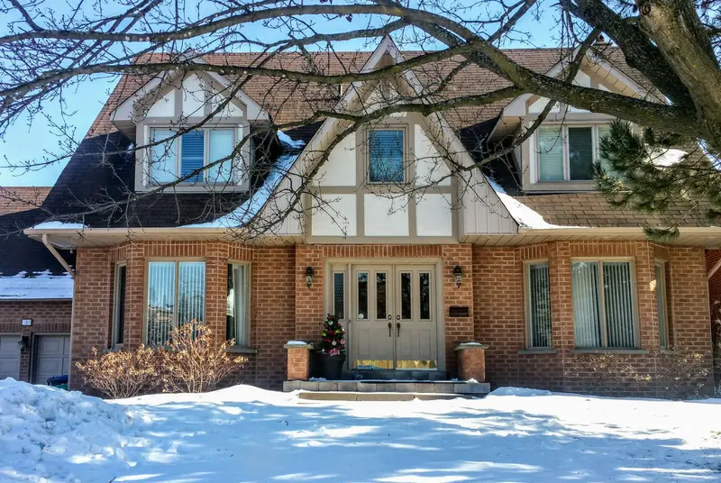 Tudor-style two-storey house with a snow-covered front lawn in winter