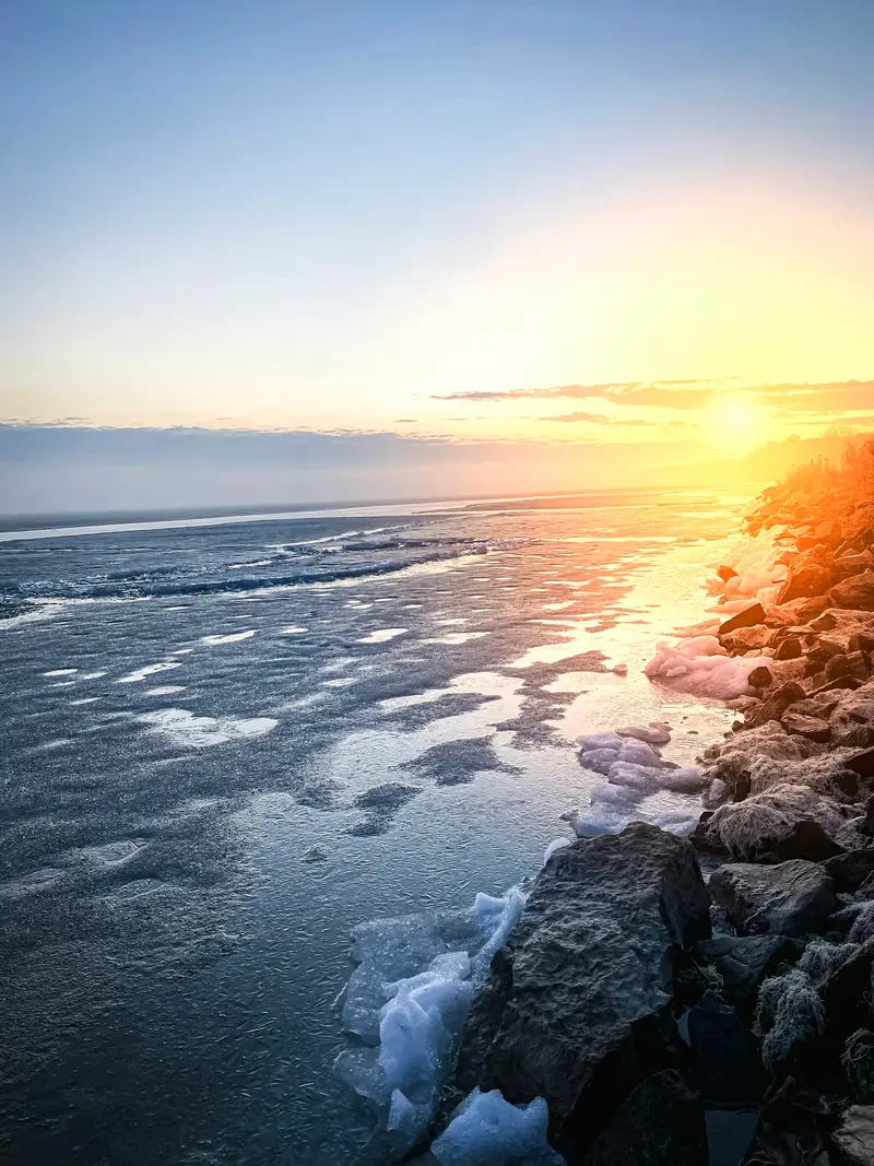 Ice breaking up along a rocky lake shore at sunset