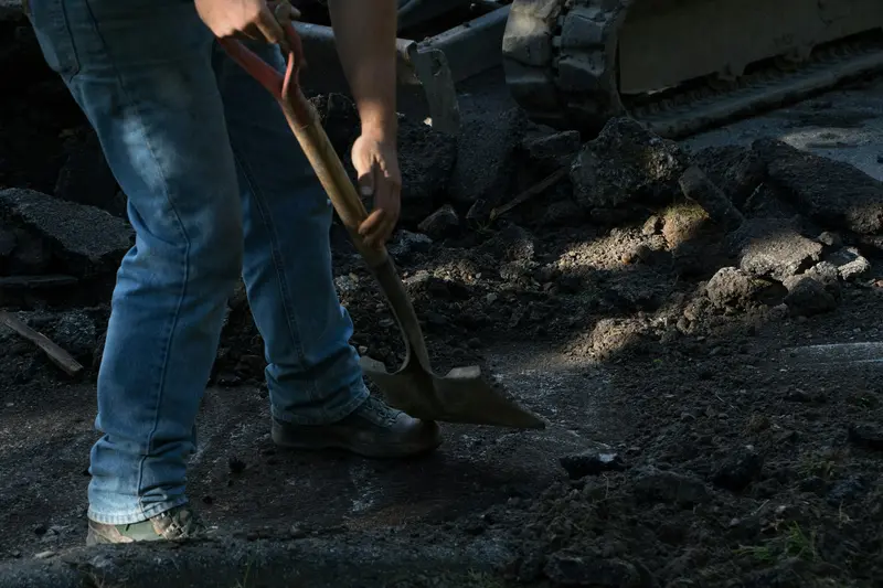 Worker digging by hand with a shovel in broken ground beside a building