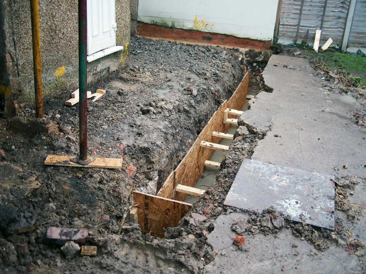 Trench with wooden formwork dug along the foundation wall of a house