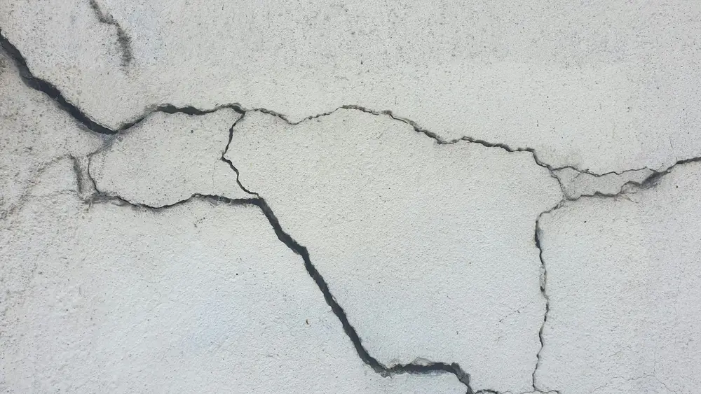 Network of dark cracks spreading across a light concrete wall surface