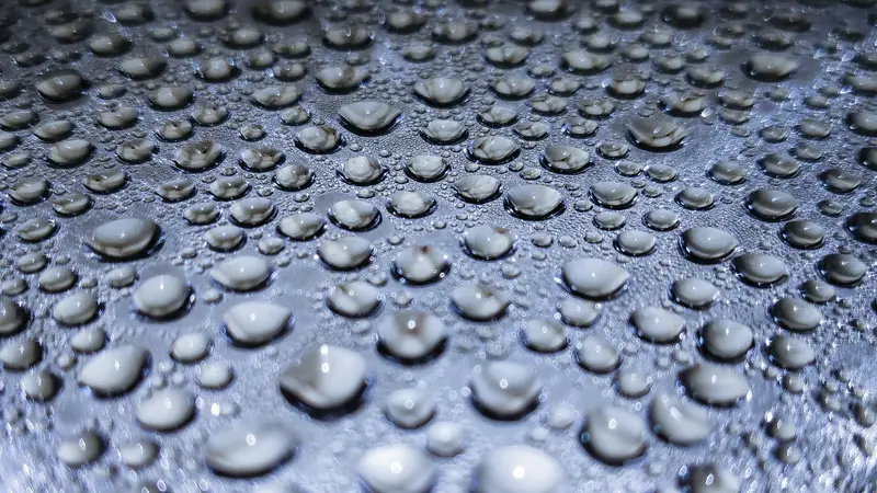 Beads of water standing on a wet grey surface