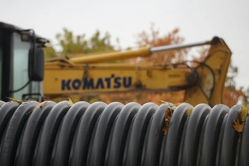 Coil of black corrugated weeping tile pipe beside an excavator bucket
